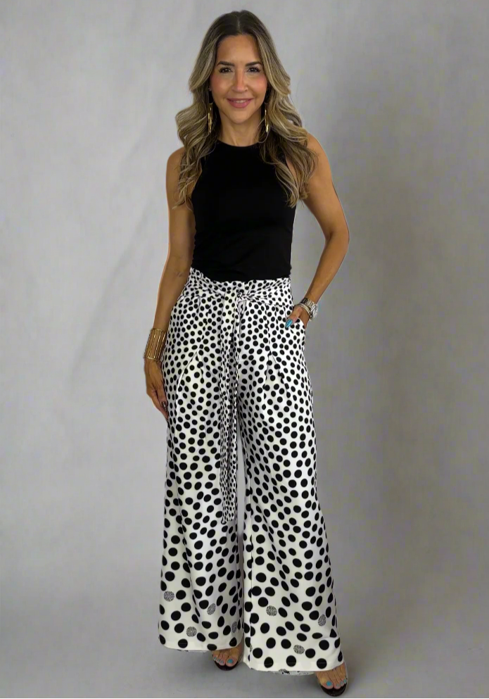 Woman wearing a black top and white pants with black polka dots on a white background