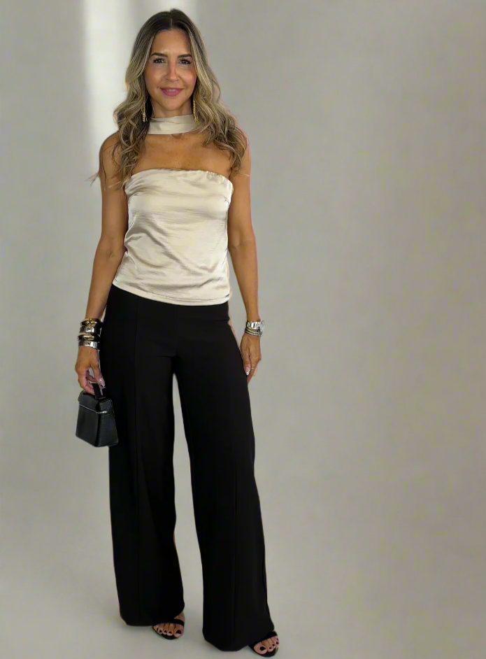 Woman wearing a beige top and black pants against a white background