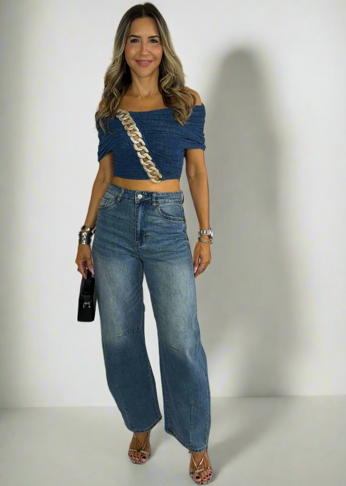Woman wearing a blue top and jeans standing against a white background