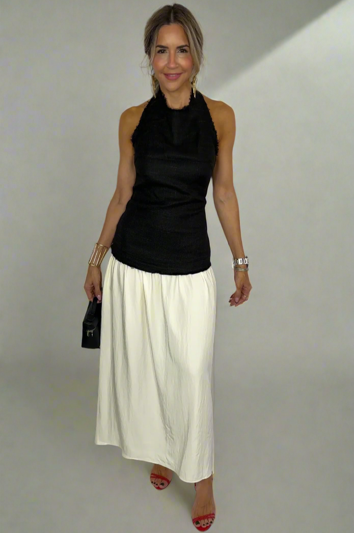 Woman wearing a black sleeveless top and white pants against a white background