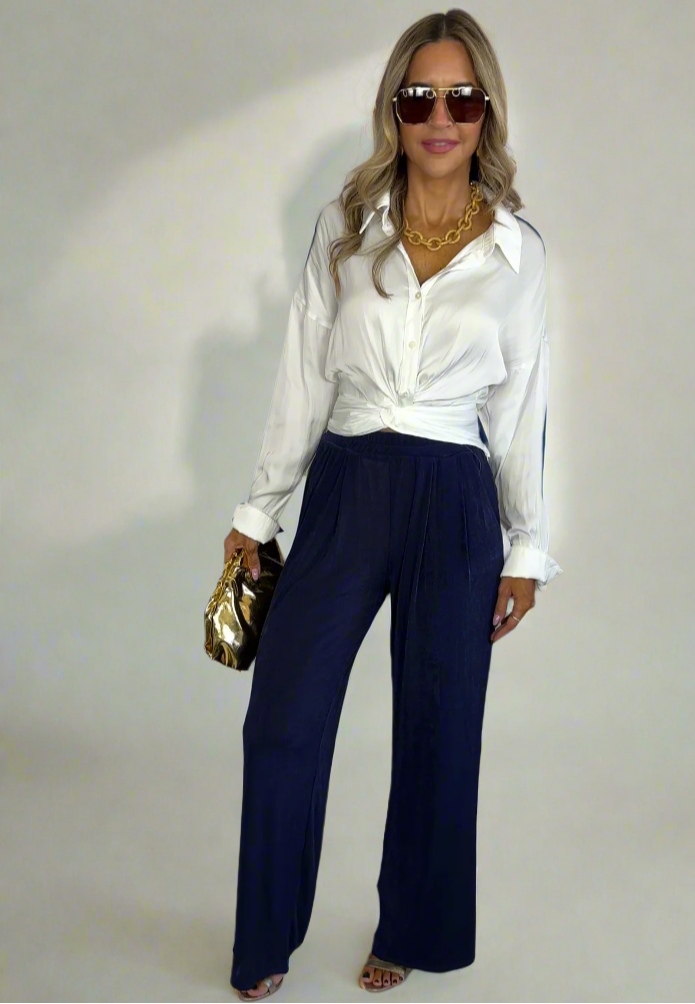 Woman wearing a white blouse and navy pants against a white background