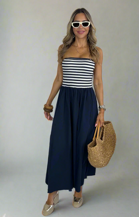 Woman wearing a striped top and navy skirt with sunglasses and a straw bag on a white background