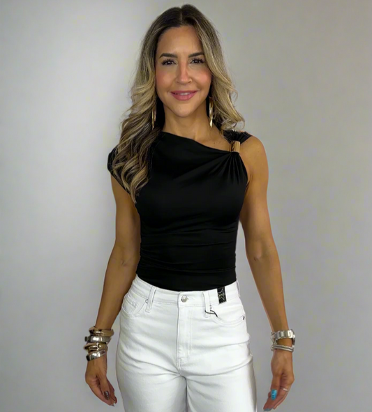 Woman wearing a black one-shoulder top and white pants on a plain background
