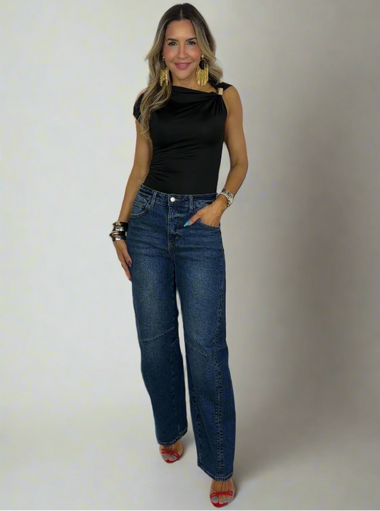 Woman wearing a black top and blue jeans standing against a white background