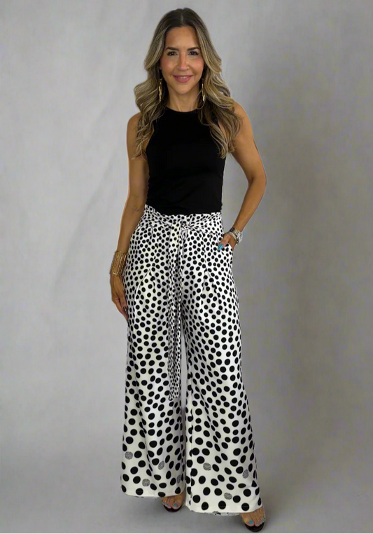 Woman wearing a black top and white pants with black polka dots on a white background