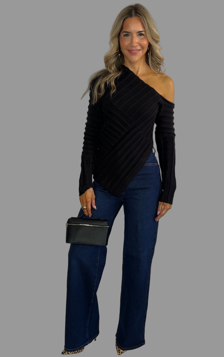 Woman wearing a black off-shoulder top and blue jeans with a black clutch against a white background
